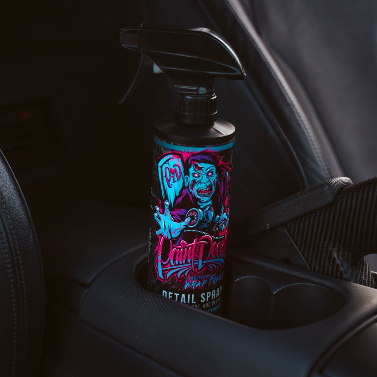 Paint Is Dead Detail Spray Gloss bottle in the cup holder of a sports car.